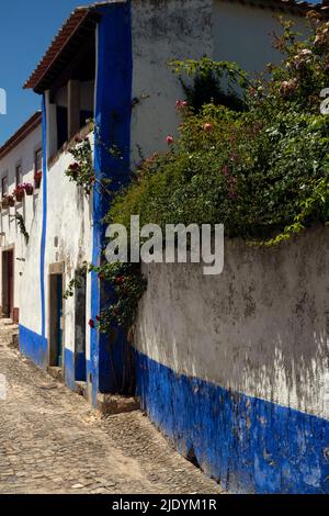 Gepflasterte Straße im Herzen der befestigten mittelalterlichen Stadt Óbidos, Centro, Portugal, gesäumt von traditionellen Häusern in typisch portugiesischem Blau und Weiß. Stockfoto