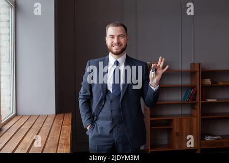 Glückliches Hausbesitzer Porträt. Froh stolzer Kerl halten bekommen Show Schlüssel von gemieteten Immobilien gekauft Haus Wohnung. Lächelnder junger Mann Makler makler Blick auf Stockfoto