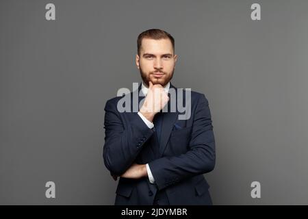 Selbstbewusster Geschäftsmann im Anzug, der auf grauem Hintergrund denkt Stockfoto