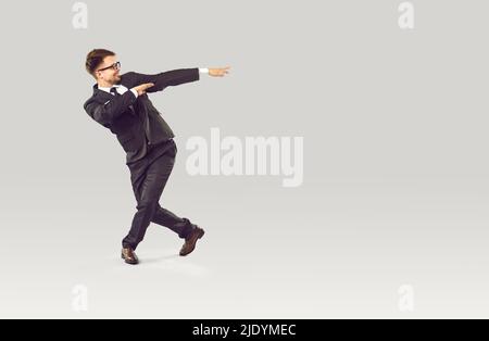 Glücklich lächelnder Geschäftsmann tanzt mit Freude und feiert Geschäftserfolg auf grauem Hintergrund. Stockfoto