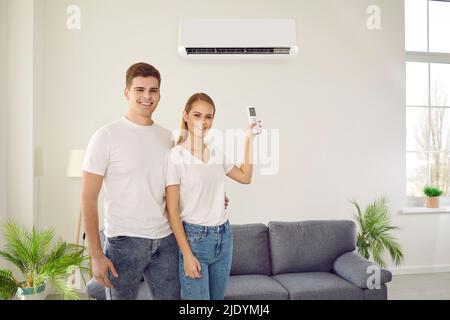 Glückliches Paar genießt es, die neu installierte Klimaanlage im Wohnzimmer ihres Hauses zu verwenden. Stockfoto