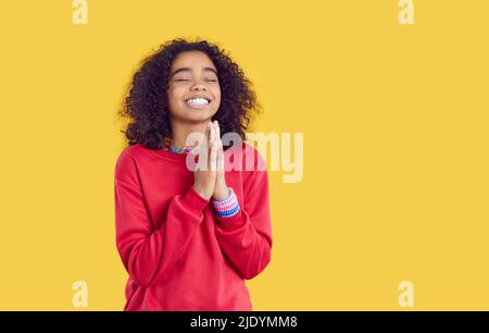 Glückliches afroamerikanisches Kind auf gelbem Hintergrund isoliert, das einen Wunsch macht oder zu Gott betet Stockfoto