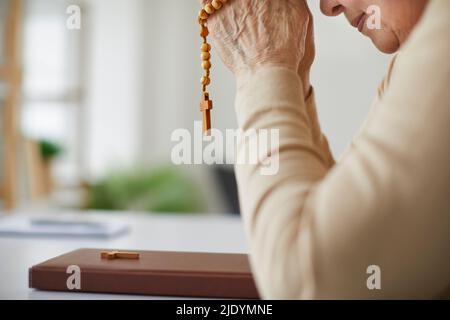 Ältere christliche Frau, die zu Gott betet und Rosenkranz über der Heiligen Bibel hält Stockfoto