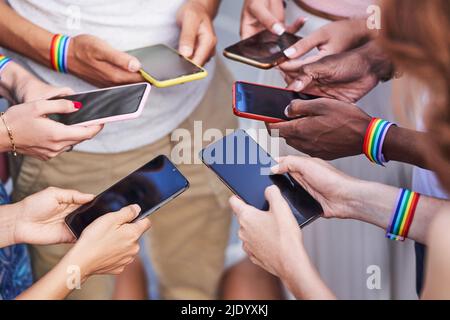 Gruppe multirassischer Menschen mit LGBT-Armbändern mit Regenbogenflagge über ihre Mobiltelefone. Diversity, LGBT, Unity und Technologiekonzept. Stockfoto