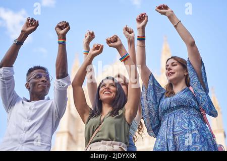 Eine Gruppe von Menschen mit mehreren Rassen, die im Freien zusammen stehen und dabei die Hände mit Armbändern mit LGBT-Regenbogenflagge heben. Konzept von Vielfalt, Gleichheit und Einheit. Stockfoto