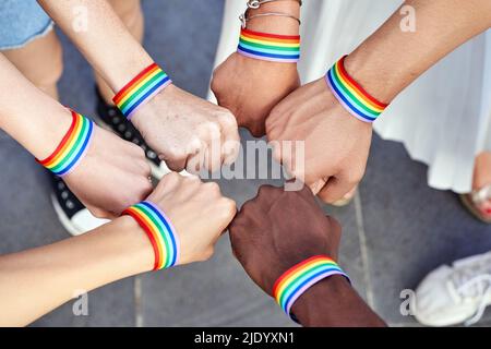 Gruppe von Menschen mit mehreren Rassen, die sich die Hände mit Armbändern mit LGBT-Regenbogenflagge zusammenlegen. Konzept für Vielfalt, Stolz, Gleichheit und Einheit. Stockfoto
