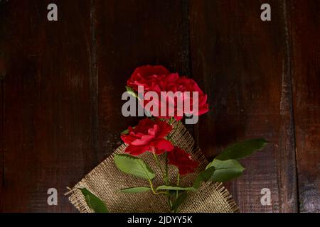 Rote Rosen Hintergrund auf Sacking auf Holzhintergrund. Geschenk, Geschenke. Speicherplatz kopieren. Stockfoto