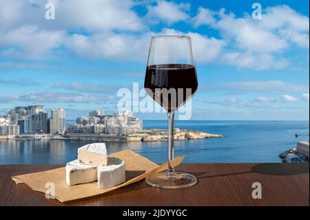 Ein Glas Rotwein mit Käse mit Blick auf die Stadt Sliema und den Hafen. Foto aus Valletta, Malta. Stockfoto