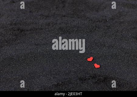 Zwei rote Herzen auf schwarzem Vulkansand. Natürlicher Hintergrund. Stockfoto