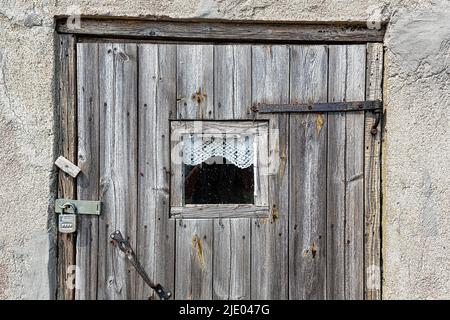 Alte braune Holztür mit Vorhängeschloss, Fenster und kleinem Vorhang, Nahaufnahme, Angelplatz, in der Saison bewohntes Dorf an der Küste, Norebod Fiskelaege Stockfoto