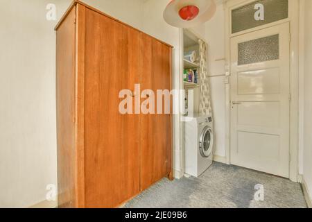 Ein geräumiges, helles und leeres Zimmer mit einem Kleiderschrank und einer Waschmaschine, in einem minimalistischen Stil Stockfoto