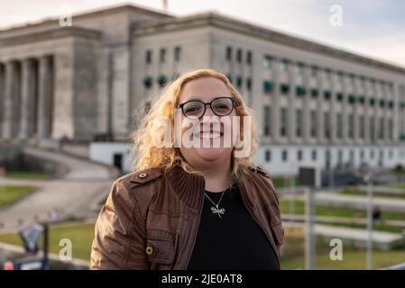 Porträt einer blonden und lockigen Plus-Size-Frau, die auf die Kamera schaut, während sie im Hintergrund einer Universität lächelt Stockfoto