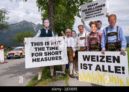 Elmau, Deutschland. 24.. Juni 2022. Demonstranten in traditionellen Kostümen mit Politikermasken stehen am Straßenrand und halten Plakate hoch. Der Gipfel G7 ist für den 26. Und 28. Juni 2022 auf Schloss Elmau geplant. Kredit: Peter Kneffel/dpa/Alamy Live Nachrichten Stockfoto