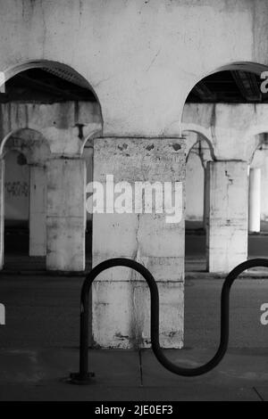 Eine Kolonnade aus Säulen in der Innenstadt, die eine Brücke in Schwarz und Weiß über sich hält. Stockfoto