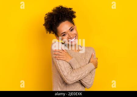 Foto von verträumt liebenswert Frau tragen beige Pullover umarmt sich isoliert gelben Hintergrund Stockfoto