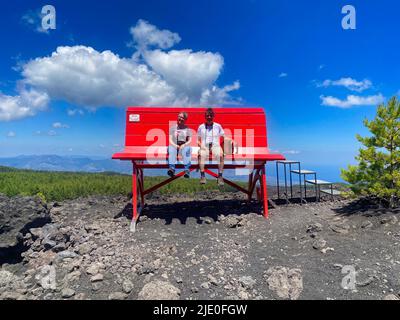 2 Menschen sitzen auf riesiger roter Bank, Big Bench Community Project, Big Bench Number 200, Etna, Grande Panchina, Linguaglossa, Sizilien, Italien Stockfoto