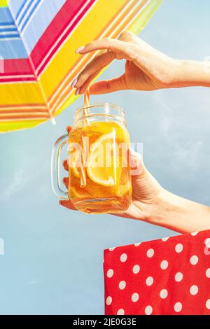 Weibliche Hand hält Glaskrug mit frostiger oranger Limonade, Cocktail auf blauem sonnigen Himmel Hintergrund. Urlaub, Glück, Sommerstimmung. Retro-Style Stockfoto