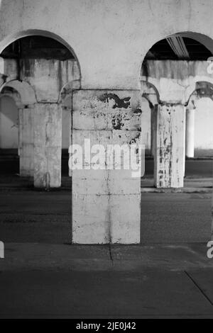 Eine Kolonnade aus Säulen in der Innenstadt, die eine Brücke in Schwarz und Weiß über sich hält. Stockfoto