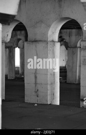 Eine Kolonnade aus Säulen in der Innenstadt, die eine Brücke in Schwarz und Weiß über sich hält. Stockfoto