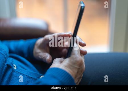 Ältere Frau hält ein Mobiltelefon und berührt den Bildschirm. Stockfoto