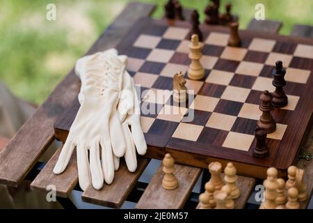 Handschuhe in der Nähe von Holzfiguren auf dem Schachbrett im Park Stockfoto