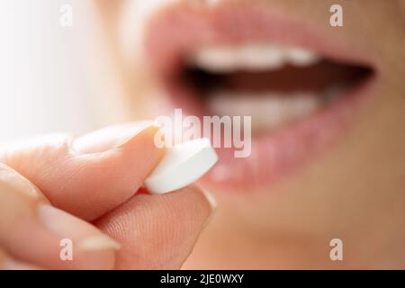 In der Nähe der weiblichen Händen, eine Weiße, runde Tabletten auf der Zunge Stockfoto