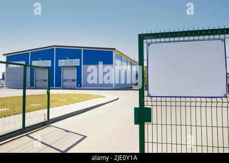 Hinter dem grünen Zaun befindet sich ein modernes Industriegebäude am blauen Himmel. Stockfoto