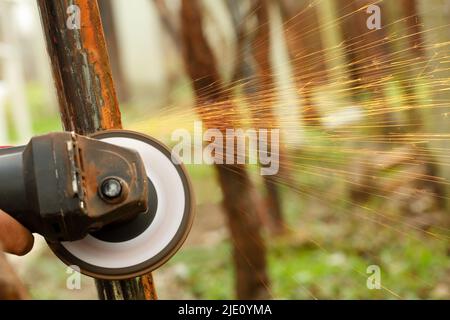 Nahaufnahme einer in Bewegung befindlichen Winkelschleifmaschine, die Rost aus einer alten Metallkonstruktion im Freien entfernt und Funken auslöst. Geringe Schärfentiefe Stockfoto
