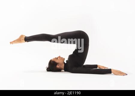 Frau in schwarzer Sportkleidung, die Yoga praktiziert, Halasana-Übung macht, Pose auf weißem Hintergrund pflügen Stockfoto