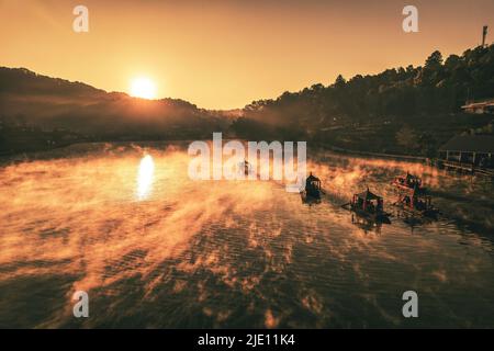 Luftaufnahme eines chinesischen Ruderbootes bei Sonnenaufgang mit Nebel über dem Ban Rak Thai Lake und dem Dorf, Thailand Stockfoto