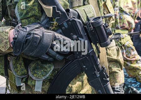 Ein bewaffneter Soldat oder Airsoft-Spieler hält ein Kampfgewehr oder Sportgewehr mit einem Zielfernrohr in den Händen Stockfoto