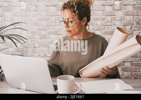Reife Schüler, die Computer und Papiere zu Hause am Schreibtisch benutzen. Bürofrau, die an einem Laptop mit Verbindung arbeitet. Selbstbewusstes Porträt weiblicher Menschen und Stockfoto