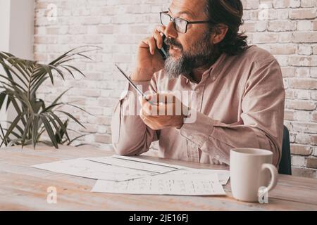 Professioneller Mitarbeiter, der am Telefon am Schreibtisch sitzt. Geschäftsmann im Gespräch auf dem Mobiltelefon. Papiernotizen und Job. Professionelle Person c Stockfoto