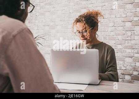 Eine Geschäftsfrau, die an der Rezeption vor einem von hinten betrachteten Mann an einem Laptop arbeitet. Konzept der Geschäftsfrau und des Kunden. Menschen arbeiten im Team zusammen. Stockfoto