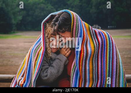 Intime lustige und glückliche Momente mit einem erwachsenen Paar bei Freizeitaktivitäten im Freien, die mit einer bunten Strickdecke im Park bedeckt sind. Mann und Frau gehen ein Stockfoto