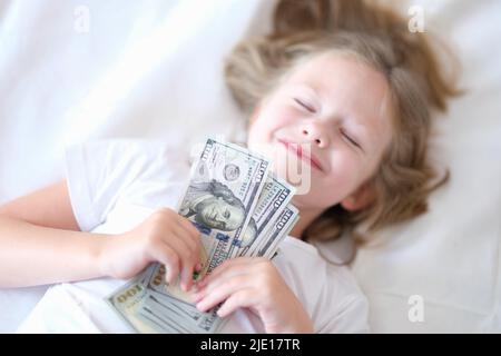 Kleines glückliches Mädchen schläft mit Cash Dollars aus der Nähe Stockfoto