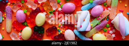 Draufsicht auf verschiedene Gelee-Süßigkeiten und Bonbons auf orangefarbenem Hintergrund, Banner Stockfoto