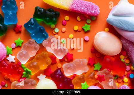 Blick von oben auf bunte Jelly Bears in der Nähe von Süßigkeiten und Dekor auf orangefarbenem Hintergrund Stockfoto