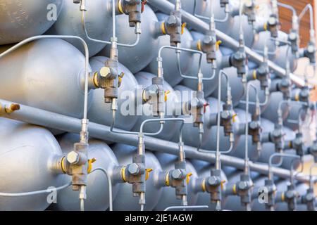 Viele verschiedene kleine Metallflaschen, die mit Gas oder Benzin gefüllt sind, werden in großen Stapeln gestapelt und von der hellen, warmen Tagessonne beleuchtet Stockfoto