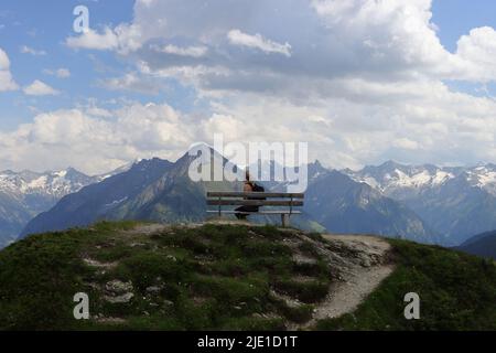 Eine Frau macht eine Pause auf einer Bank hoch über den Bergen Stockfoto