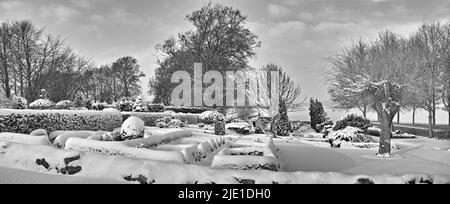 Düsterer Friedhof in einer monochromen Winterlandschaft. Schneebedeckte Grabsteine vor einem grau bewölkten Himmel. Schwarz und weiß leer mattiert Friedhof und Stockfoto