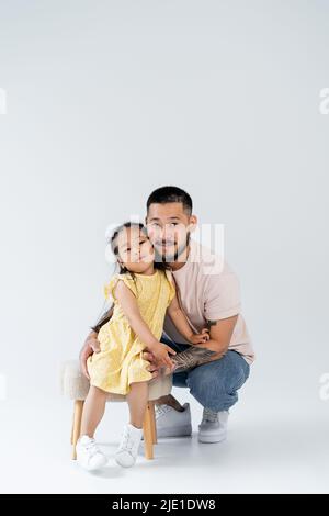 Volle Länge der glücklich asiatische Mädchen im Sommerkleid stehen in der Nähe Vater auf grau Stockfoto