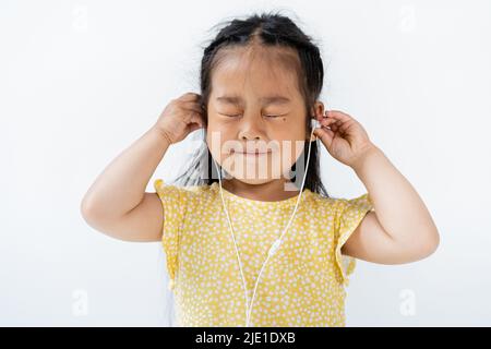 Zufrieden asiatische Mädchen mit geschlossenen Augen tragen kabelgebundene Kopfhörer isoliert auf grau Stockfoto