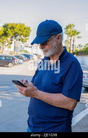 Älterer Mann in legerer Kleidung, der Smartphone benutzt und vor der Stadt steht. Stockfoto