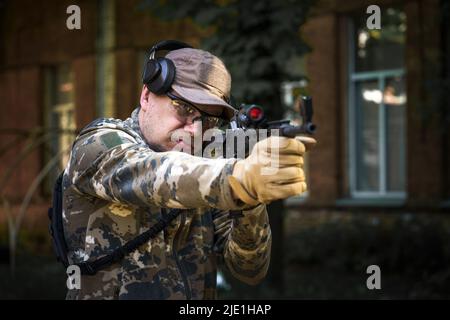 Cadet Trainingskurs, Mann mit Waffe in militärischer Uniform taktischer Gehörschutz Headset. Ausbildung im Schießbetrieb. Zivilpolizisten in taktischem Trainingskurs. Selektiver Fokus. Stockfoto