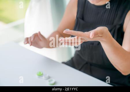 Kontaktlinse befindet sich am Zeigefinger des Mädchens. In der Nähe befindet sich ein Behälter für Linsen. Nahaufnahme, Seitenansicht Stockfoto