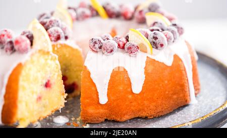 Schritt für Schritt. Schneiden Sie den mit Zuckercranberries und Zitronenkeilchen dekorierten Zitronenkuchen mit Preiselbeeren. Stockfoto