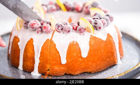 Schritt für Schritt. Schneiden Sie den mit Zuckercranberries und Zitronenkeilchen dekorierten Zitronenkuchen mit Preiselbeeren. Stockfoto