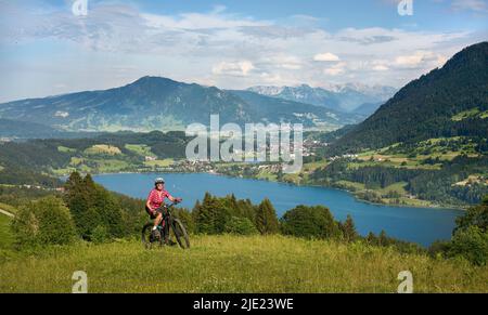 Schöne ältere Frau auf ihrem elektrischen Mountainbike auf den Bergen über dem Alpsee bei Immenstadt, Allgau, Bayern, Deutschland Stockfoto