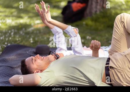 Ein romantisches Paar junger Leute, die im Park auf Gras liegen. Sie sehen glücklich aus. Blick von der Seite Stockfoto